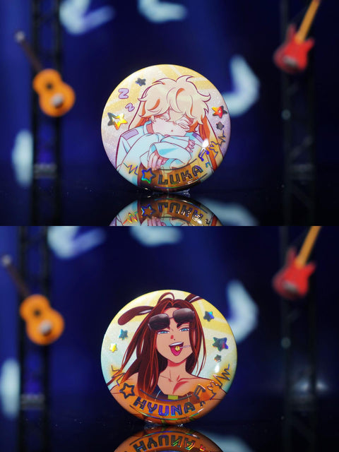 Close-up photography of the Luka and Hyuna badges, highlighting the character art against a vibrant holographic glitter background.