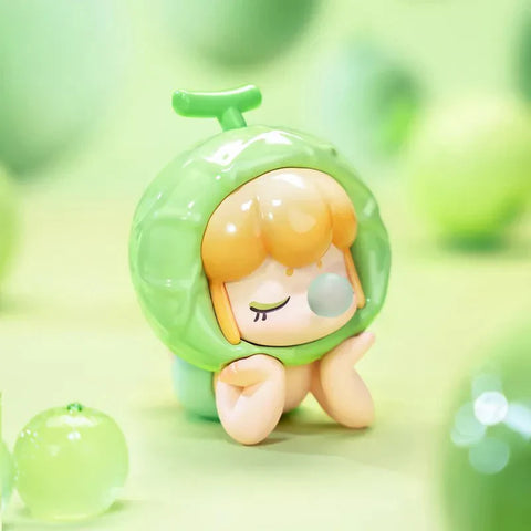 This image features a charming collectible figurine from the Baby Nanci Fruits Series Blind Box collection. The figure has a peaceful expression, with its eyes closed and hands resting on its cheeks. It wears a glossy, light green cantaloupe-inspired headpiece, complete with a textured rind-like design and a small stem on top. The character’s short, wavy orange hair complements the fruit theme beautifully. The background is a soft, pastel green, decorated with translucent melon-like elements.