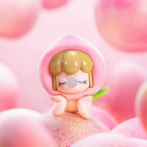 This image showcases an adorable collectible figurine from the Baby Nanci Fruits Series Blind Box collection, featuring the secret hidden chaser design. The character has a calm, dreamy expression with closed eyes and hands gently resting on its cheeks. It wears a soft, fuzzy-textured, pastel pink peach-inspired headpiece with a tiny green leaf attached to the side. The figure’s short brown hair peeks out from the hood, adding charm to its delicate appearance. The background is a dreamy pink hue.