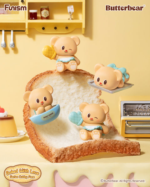 A group of Butterbear “Baked With Love” figures posed on a giant slice of bread, each styled for baking play. One bear winks holding an oven mitt, another lies on a baking tray with a bow, while others rest in a cream cheese tub or pose as a cuddly loaf. Whimsical bakery details enhance the cozy, cubby theme.