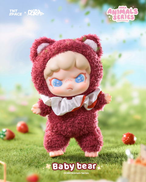A plush figure dressed as a deep red bear with fuzzy textured suit, white chest ruffle, and pointed ears. The doll has pale skin, wide blue starry eyes, and a slightly pouty expression. It stands barefoot on grass with strawberries scattered nearby, evoking a whimsical picnic scene.