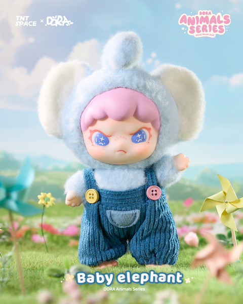 A pastel plush doll in a soft blue elephant hood with large floppy ears and matching fuzzy suit. It wears corduroy blue overalls with colorful buttons, paired with short pink hair and bright star-filled eyes. The figure stands on grassy terrain surrounded by playful flowers and pinwheels.