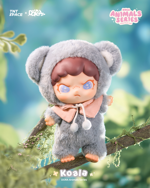 A plush doll in a soft gray koala outfit with rounded ears and a peach-pink hood tie. Its brown hair frames a pouty expression highlighted by bright blue sparkling eyes. The figure balances on a tree branch surrounded by lush greenery, resembling a whimsical forest encounter with a gentle marsupial.