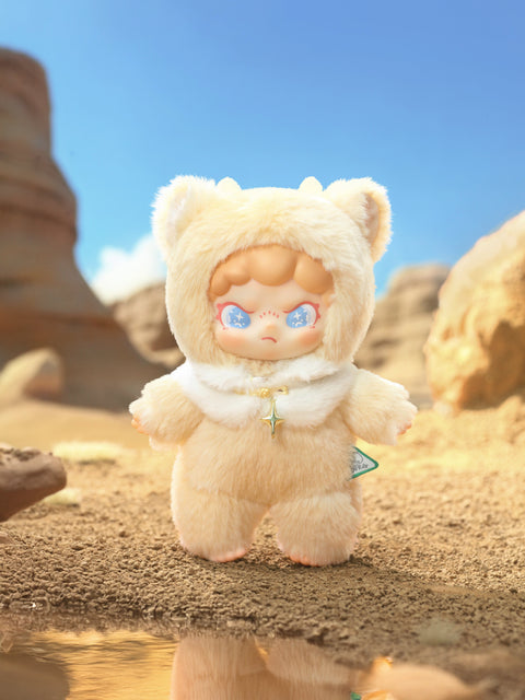 Fluffy cream bear‑hood figure with blue starry eyes and a gold star pendant stands on cracked desert earth. Warm sunlight, eroded stone formations, and a tiny reflective puddle create a sun‑baked canyon backdrop that highlights the toy’s soft textures.