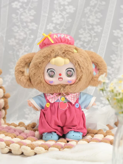 A 400% Doubao Apple Monkey figure wears a fuzzy brown monkey hood with round ears, a red hat embroidered with “Apple,” and bright red overalls decorated with a stitched apple patch. Its wide eyes and playful expression capture Doubao’s signature charm, standing on a cozy knit rug in a soft indoor display.