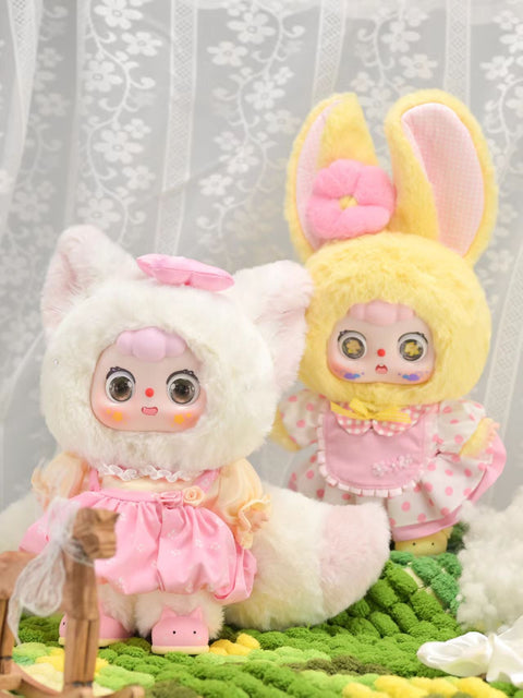 Doubao Rose Fox and Honey Rabbit stand side by side, one in a fluffy white fox suit with a pink dress and bow, the other in a soft yellow bunny hood with long ears and a dotted apron dress. Together, their plush textures and pastel designs highlight the playful variety of the series.