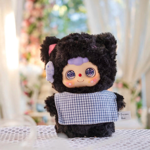 Kitten Doubao plush in a velvety black fluffy suit with soft cat ears and a purple bow. It wears a gingham bib and displays twinkling cat-themed eyes with sweet facial details. The plush combines gothic cuteness with playful feline charm for a standout character design.
