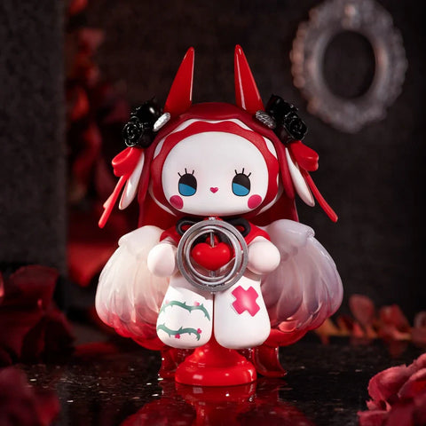 A detailed figurine from the "Emma Secret Forest: Beloved Series" stands in a dark, romantic setting with red rose petals. The character wears a red hood with pointed ears, black rose accessories, and translucent white wings. It holds a circular frame with a red heart inside, symbolizing devotion. Its white outfit features thorny vines and a red cross, adding a mystical, gothic charm. The background’s deep tones and ornate frame enhance the dramatic, fairytale-like atmosphere.