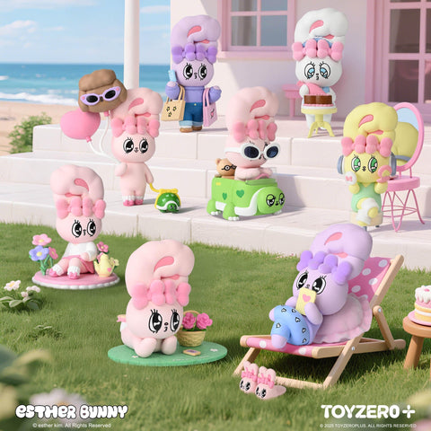 A group of pastel-colored Esther Bunny figurines enjoy a seaside holiday scene outside a pink beach house. Each bunny has expressive eyes and big bows, shown in playful poses like gardening, lounging, traveling with luggage, eating cake, and relaxing on the lawn.