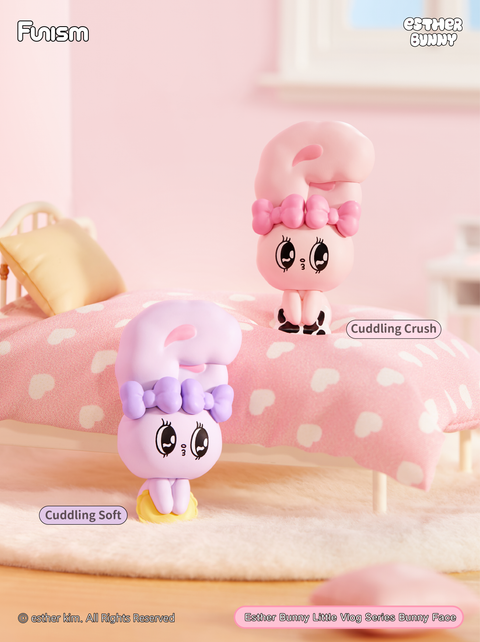 Bedroom scene with two bunnies, one lilac and one pink, in cuddly poses on a bed and rug. Surrounded by pastel heart-pattern bedding, the figures embody coziness, comfort, and affection.