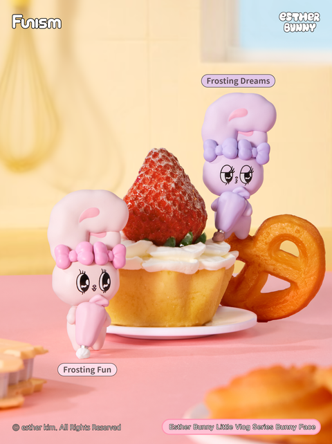 Kitchen baking setup with two bunnies decorating a cupcake with frosting. One bunny pipes whipped cream while another admires the strawberry topping. The scene highlights sweet, playful dessert-making fun.