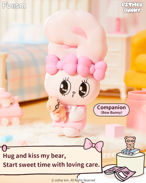 A pastel bunny figure named Bow Bunny stands in a soft pink room, hugging a tiny brown teddy bear. The bunny wears a pink bow and light pink dress, with shiny black eyes and round cheeks. The cozy setting includes a bed, toy train, and fuzzy carpet under warm morning light.
