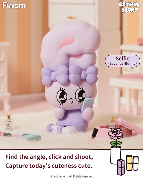 A lavender bunny figure named Lavender Bunny kneels on a fluffy rug holding a phone with a pink heart. The bunny has a large lilac bow and sits surrounded by mini bottles and makeup items in a softly lit bedroom decorated in warm pastel shades.