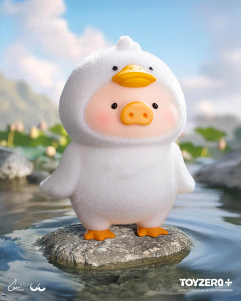 A LuLu the Piggy figure in a fluffy white duck costume with orange webbed feet and a duck face hood. It stands on a rock in a pond, surrounded by lotus flowers and a bright blue sky.