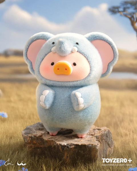 A LuLu the Piggy figure in a light blue elephant costume with large ears, a trunk, and tusks. The figure is posed on a rock in a golden grassy plain with trees and a wide sky in the distance.