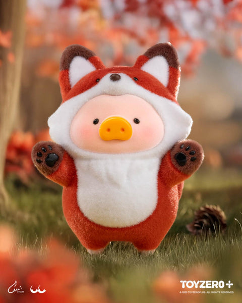A LuLu the Piggy figure in a vibrant red fox costume with white chest and muzzle details, big pointed ears, and tiny paw prints on its hands. It stands on a forest floor with warm autumn leaves scattered around.