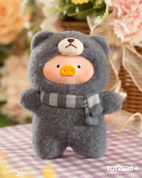 A cozy plush from the "LuLu The Piggy: Joyful Time Series" features LuLu dressed in a fluffy dark gray teddy bear costume with a tiny bear face on the hood. It wears a matching striped scarf, adding to its warm and cuddly appeal. With a soft pink blush and round piggy snout, the plush exudes charm. The background, with a wicker basket, pastel flowers, and a gingham tablecloth, enhances the inviting and nostalgic atmosphere of this adorable collectible.