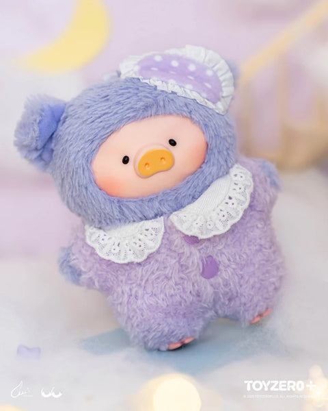 A plush pig character in a fuzzy lavender bear suit stands against a soft pastel backdrop. The suit has rounded ears, a white lace collar, and two purple buttons. A polka-dot sleep cap with ruffled trim rests on one ear. The pig’s gentle expression and cozy textures create a calm, bedtime-inspired appearance.
