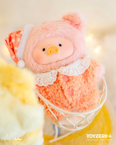 A plush pig dressed in a peach-colored fuzzy suit sits in a white basket. The suit features floppy ears, a lace collar, and pink buttons. A matching peach sleep hat with white star patterns rests on its head. Warm lighting and soft surrounding textures emphasize a charismatic, comforting bedtime design.