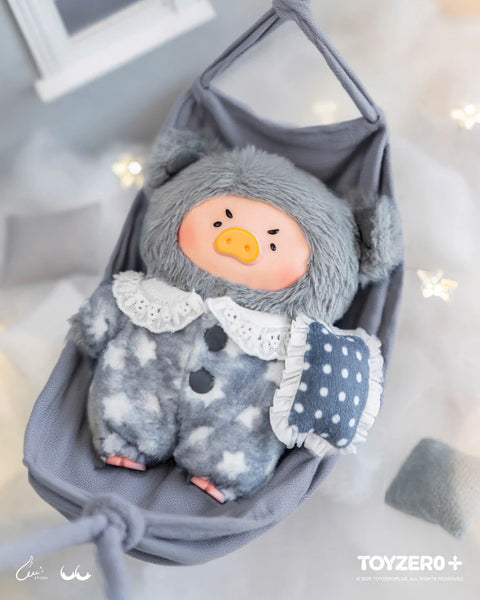 A gray plush pig in a star-patterned bear suit rests in a hanging fabric cradle. The suit features white star shapes, fuzzy ears, and a lace collar. The pig holds a polka-dot pillow with ruffled trim. Its furrowed brow expression and nighttime setting create a dramatic hidden-chaser themed appearance.