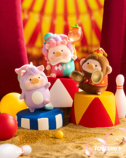 Three pig figurines pose on colorful circus pedestals. One wears a soft pastel unicorn costume, another is a clown with multicolored hair holding a translucent balloon, and the third wears a brown cymbal-monkey suit with gold cymbals. Red curtains and golden sand form the circus-style backdrop.
