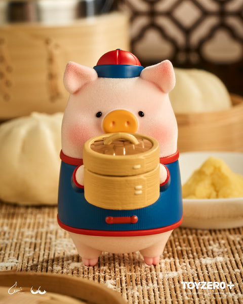 A flocked LuLu the Piggy figure in a blue traditional Chinese tunic holding a two-tier bamboo steamer. The setting features large steamed buns and traditional bamboo kitchenware on a woven mat.