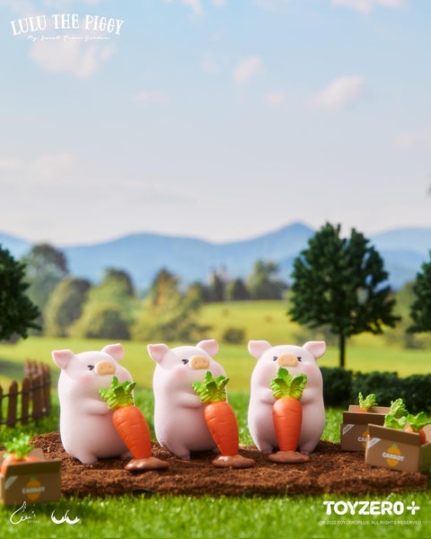 Three LuLu piggies in the soil, each with a determined expression while pulling a large orange plush carrot from the ground.