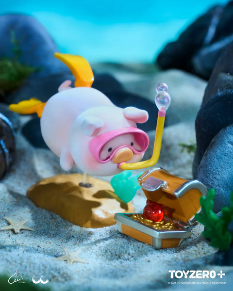 A LuLu the Piggy figure from the Ocean Series by 52TOYS and ToyZero+ is shown underwater in a diving scene. The pig wears pink goggles, a yellow snorkel, and yellow flippers while swimming toward an open treasure chest filled with gold and a red gem. Surrounded by sand, starfish, and rocks, the figure captures an adventurous moment of underwater treasure hunting in a whimsical, oceanic diorama.