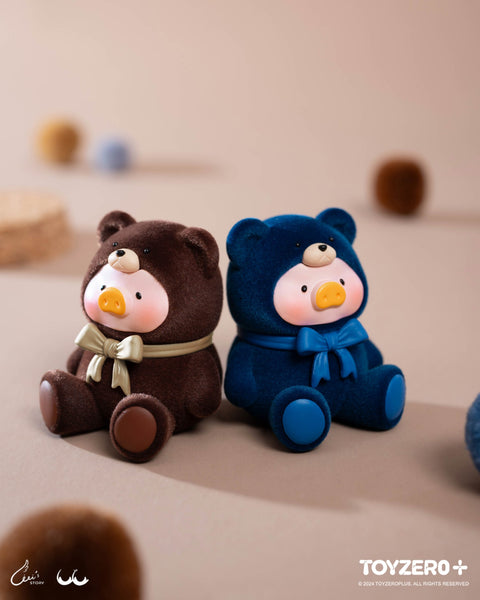 Brown and navy teddy-clad piggy figures sit side by side. Their fuzzy flocked textures and satin bows create a cozy, plush look against a neutral backdrop.