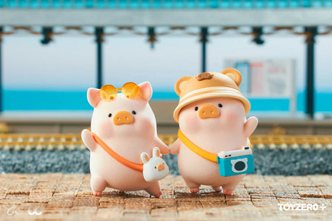 Two LuLu the Piggy figures from the Travel Series by 52TOYS and ToyZero+ stand side by side on a sunlit train platform. One pig wears orange sunglasses and carries a bunny-shaped bag, while the other sports a bear hat and a yellow strap with a teal camera. They hold hands, ready for their travel adventure. The ocean and tracks form a scenic backdrop, capturing the excitement of checking in and setting off on a summer journey.