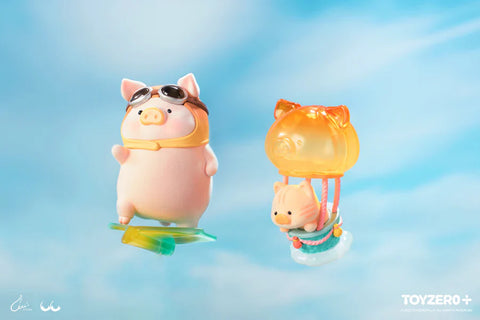 Two special edition LuLu the Piggy Travel Series figures from 52TOYS and ToyZero+ float in a dreamy sky. One pig wears aviator goggles and a scarf, riding a translucent green board as if gliding through the air. The other rides in a whimsical orange cat-shaped hot air balloon with a cloud base. These secret and super secret chaser figures capture a sense of wonder and flight in a pastel sky backdrop.