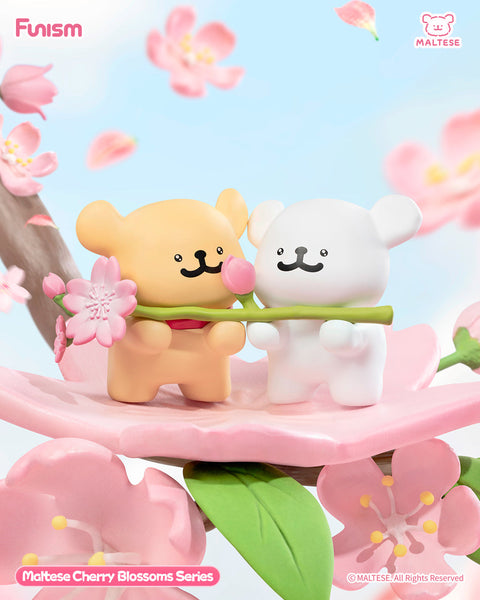 Two Maltese bear figures stand on a giant pink cherry blossom petal, one tan and one white, holding a stem with a pink flower between them. Blossoms float around in the sky, creating a dreamy spring scene.