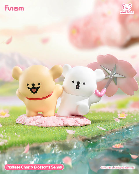 Two Maltese bears stand together on a pink blossom patch, the tan one happily leading while the white one waves a pink cherry blossom star wand. They stand beside a sparkling river with petals floating by.