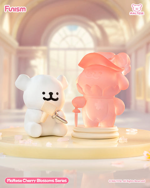 A white Maltese bear holds a sculpting tool while carving a translucent pink cherry blossom statue of another Maltese bear. They stand on a pastel pedestal inside a glowing indoor spring display.