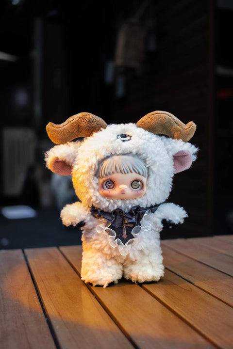 White curly plush doll with brown ram horns, a third eye on its forehead, and a black lace collar. One eye has a plus sign and the other a minus sign.