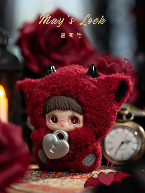 A plush figure is positioned on a rug wearing a deep red fuzzy hood with pointed ear shapes and small black horn details. The character holds a metallic silver heart-shaped lock at the front. The face has short brown bangs, large dark eyes, and a neutral expression. Background elements include a red rose, a pocket watch, candlelight, and dark romantic decor.