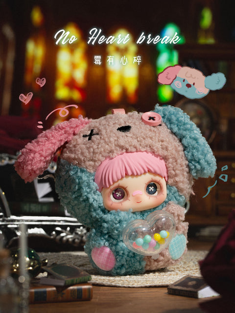A hidden chaser plush figure wears a two-tone fuzzy hood in muted pink and teal with floppy ear shapes and stitched facial symbols on the hood. The character has pink bangs, large eyes with decorative details, and holds a clear heart-shaped container filled with colorful beads. The scene includes books, candles, and dim ambient lighting with a melancholic tone.