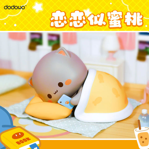 A gray cat named Huihui lies cozily on a yellow pillow, wrapped in a fish-print blanket, holding a blue phone with a paw icon, inside a warm bedroom.