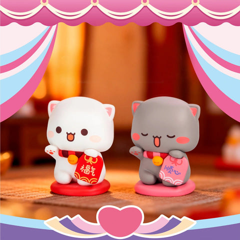 Peach and Goma posing as lucky cats with red and pink traditional blessing pouches.