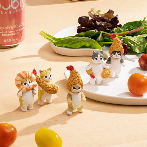 Lifestyle display image of the complete Mofusand Shrimp Meow Series arranged on a light wooden table with plates, vegetables, and kitchen props. Multiple cat figures in shrimp costumes are posed standing and interacting around dishes, creating a playful food-themed scene. The figures show detailed shrimp textures, soft color variations, rounded paws, and expressive eyes, highlighting the series’ cozy aesthetic and charming, humorous presentation.