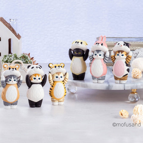 Six standing cat figurines appear against a plain white background, each holding an oversized animal-themed hood above their heads. Costumes include a yellow dog, pink bunny, brown bear, white panda, yellow tiger, and a white-and-black cow. All figures have upright poses, rounded bodies, and textured fur detailing.
