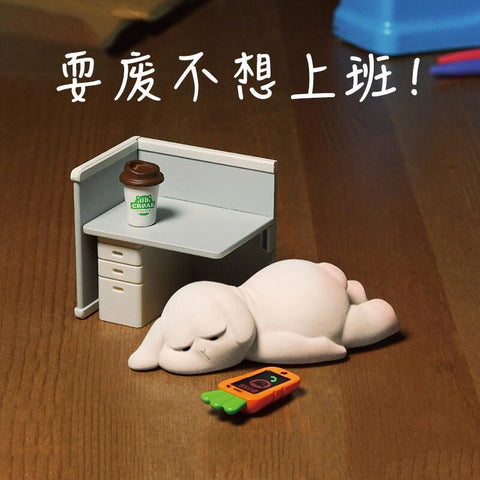 A bunny figure lies flat on the floor in exhaustion beside a desk with a pink rabbit clock and empty drink cans, humorously representing laziness and refusal to work.