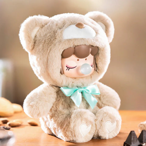 A charming collectible figurine from the "Nanci Colorful Chocolate Cutie Bears" plush series features a character dressed in a soft, hazelnut-colored bear suit with a mint green satin bow. The figure has a peaceful expression with closed eyes and a bubblegum bubble, while heart-shaped details adorn its plush paws. Seated on a wooden surface with nuts and chocolate nearby, the warm, golden lighting enhances the cozy and sweet ambiance of this delightful scene.
