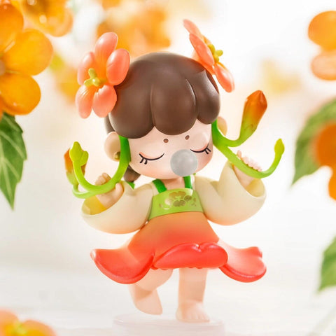 A figurine from the Nanci “Flower Stories” blind box series inspired by the campsis flower. The character has brown hair with two large orange blossom accessories and wears a light yellow top with green trim and a flared red skirt shaped like petals. With eyes closed and a bubble at her lips, she holds green flower stems in both hands while surrounded by blooming campsis vines, capturing a lively and cheerful summer energy.