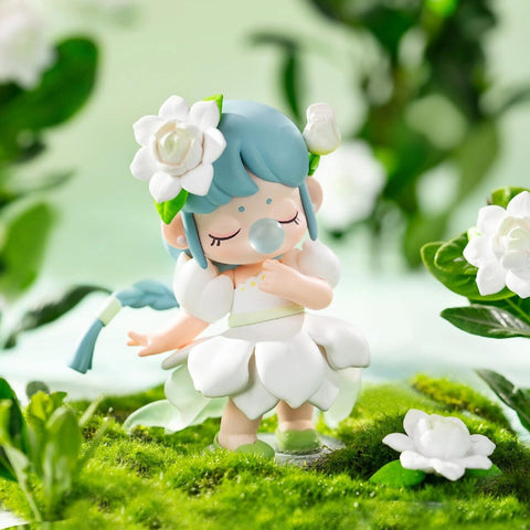 A figurine from the Nanci “Flower Stories” blind box series inspired by the gardenia flower. The character has light blue hair styled in a braid and wears a white petal-shaped dress with puffed sleeves. A gardenia bloom decorates her hair as she stands with eyes closed and a bubble at her lips, surrounded by lush green moss and blooming white gardenias, exuding a pure, fresh, and elegant charm.