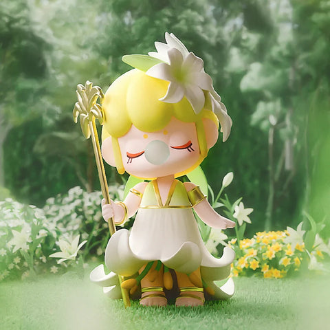 A graceful collectible figurine from the "Nanci Secret Garden" series features a character inspired by the elegant lily flower. She wears a flowing white and green dress resembling delicate petals, with golden accents and a matching floral crown. Holding a golden staff adorned with lily motifs, she exudes a serene and regal aura with closed eyes and a bubblegum bubble. Set against a lush garden backdrop filled with blooming lilies, this figure embodies purity, beauty, and tranquility.