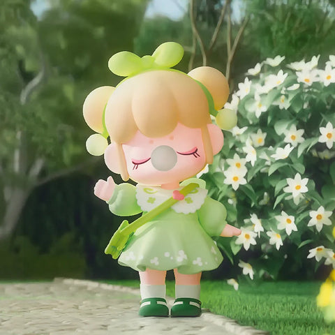 Nanci in a cute green dress with a matching green headband up top. There are pretty flowers in the background.