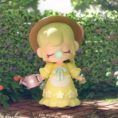 Nanci in a yellow garden dress with a brown hat on top of her head. In her right hand is a watering can.