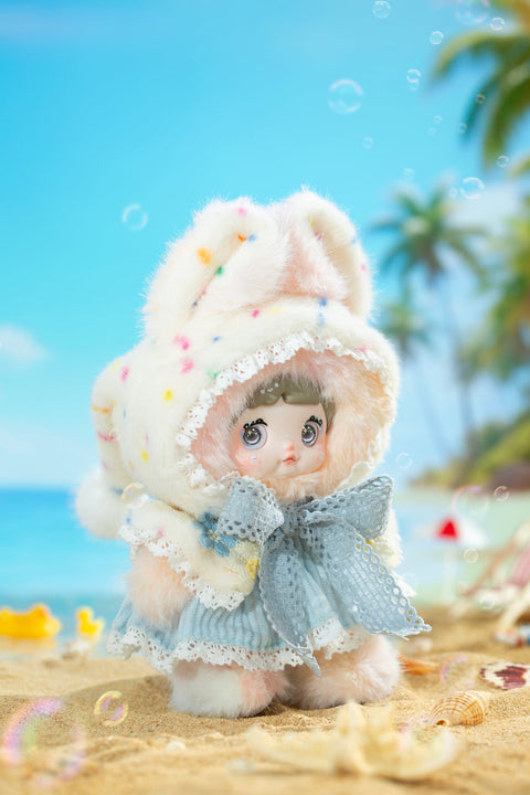 Plush figure in a pastel pink outfit with long floppy bunny ears, lace accents, and soft layered fabrics, posed on a warm beach scene at sunset. The character’s gentle expression, glossy eyes, and warm lighting emphasize a sunny, glowing weather theme.