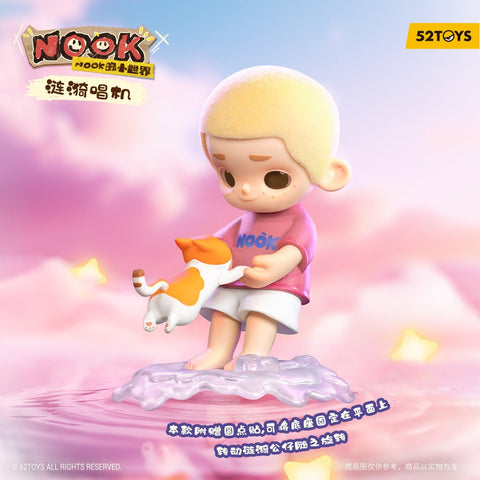 A child figurine with short blond hair stands barefoot on a rippling translucent lavender base, gently holding an orange-and-white cat out in front. The child wears a pink Nook T-shirt and white shorts. Soft pink clouds, yellow star shapes, and dreamy pastel lighting create a floating sky-like background.